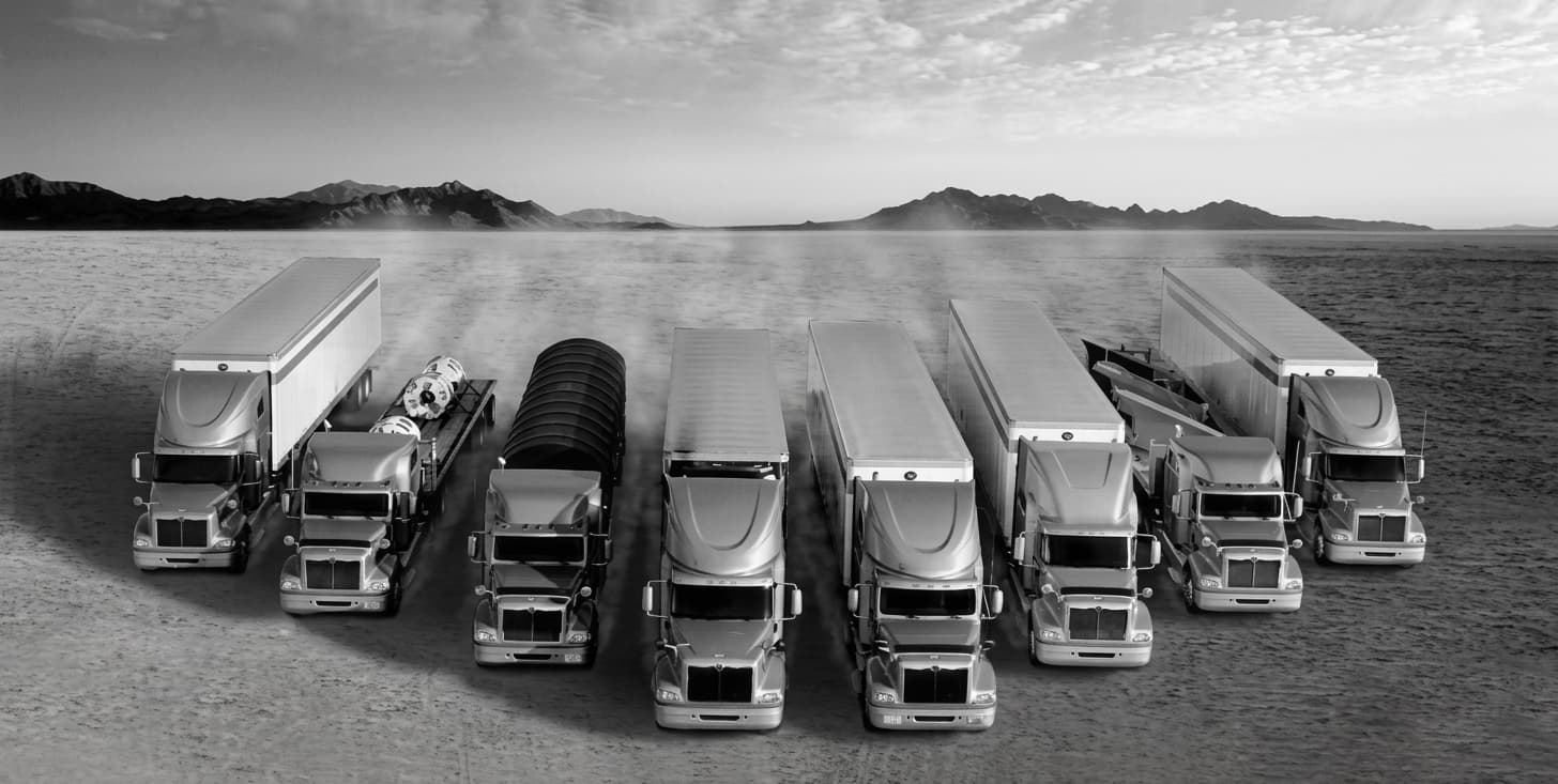 A wide-angle, industrial photograph of a massive fleet of modern semi-trucks parked in a highly organized grid at a logistics terminal at dawn